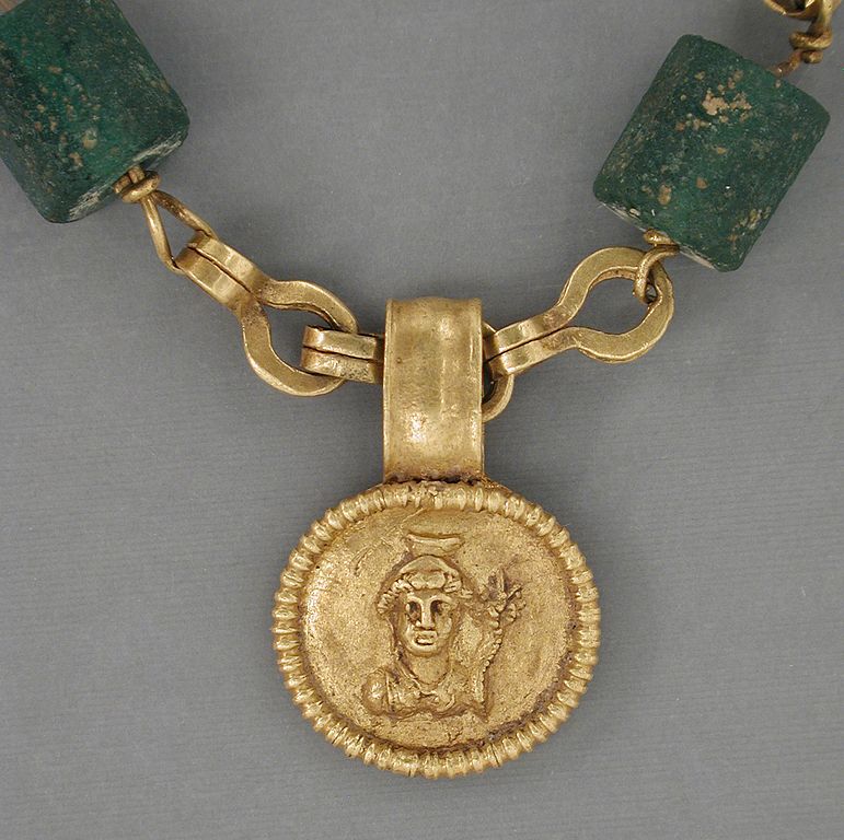 This Egyptian necklace dates from 30 BCE – 300 CE and features green glass beads. “Gold Necklace with Medallion Depicting a Goddess LACMA 50.22.20.” Public Domain.